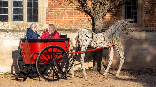 A small, red-painted governess cart and wooden horse hitched to the cart stand in the Service Courtyard